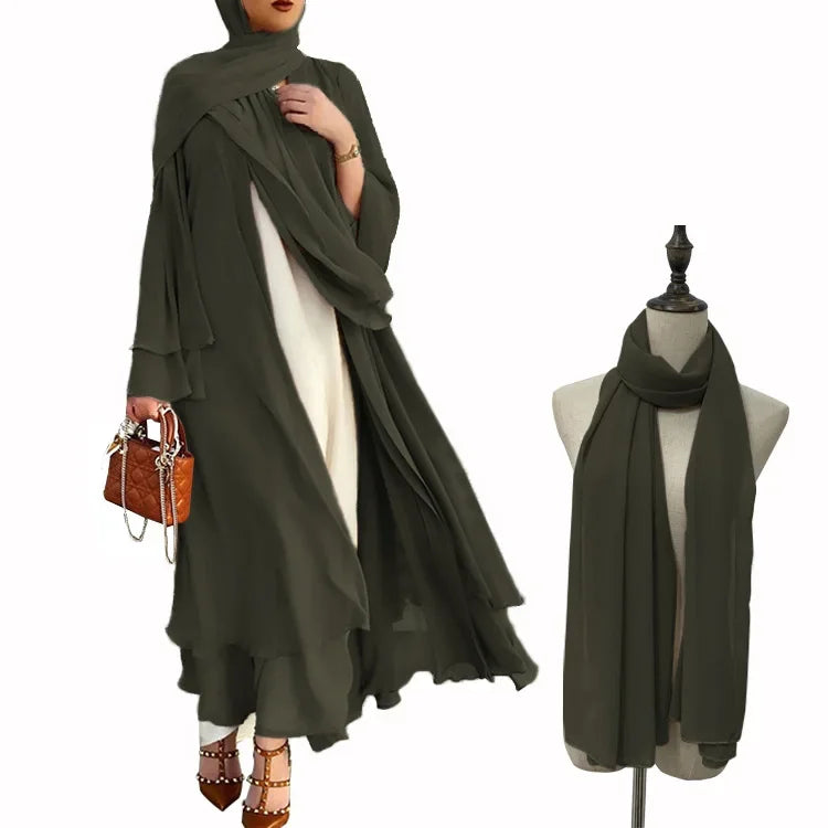 Woman wearing a green abaya with a matching scarf on a mannequin, holding a brown handbag.
