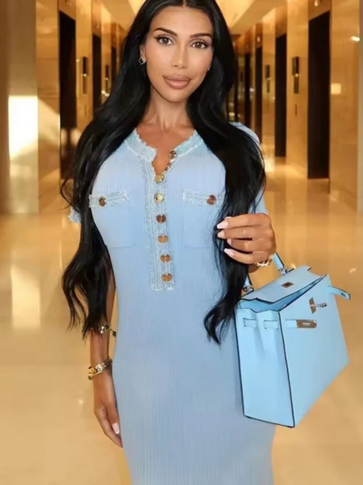 Woman in a light blue dress holding a matching handbag in an elegant hallway.