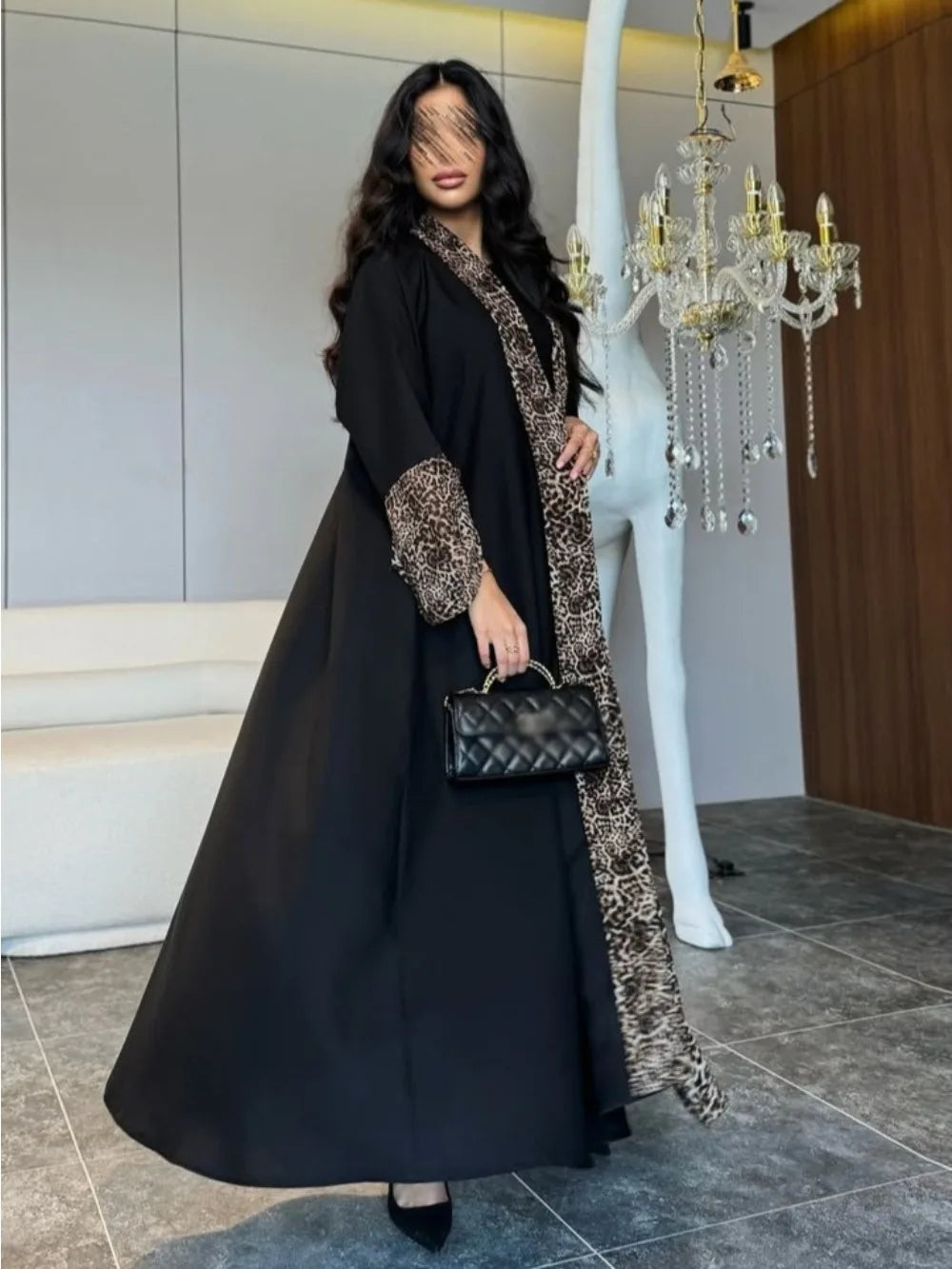 Woman in a black and leopard print dress holding a black handbag indoors.