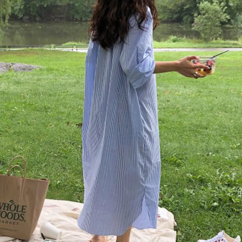 Person in a blue striped dress standing outdoors with a Whole Foods bag on a blanket.
