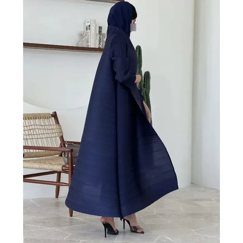 Person wearing a navy blue abaya in a room with a chair and shelf.