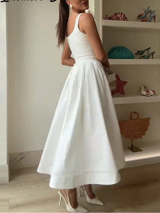 Woman wearing a white dress standing in front of a shelf with various items.