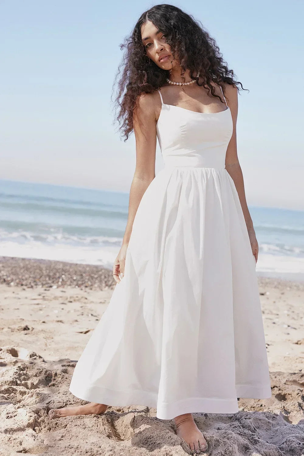 Woman in a white dress standing on a beach with ocean in the background