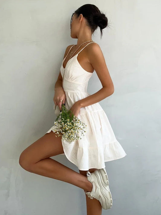 Woman in a white dress holding flowers against a plain background