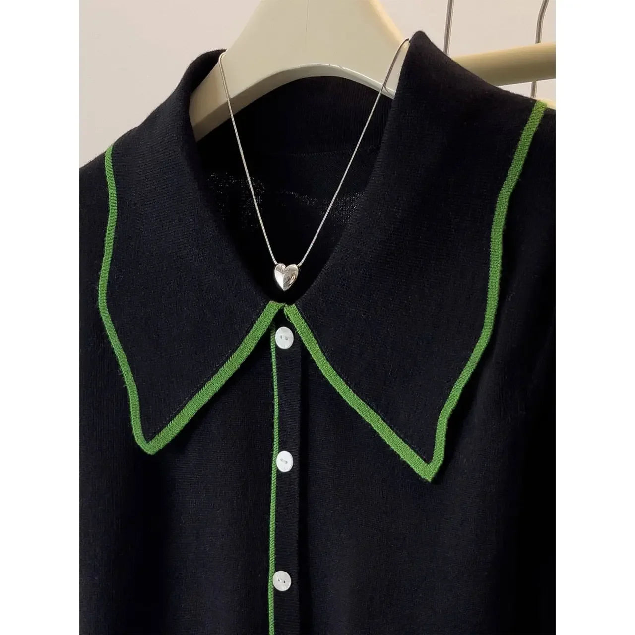 Black shirt with green collar and white buttons on a hanger