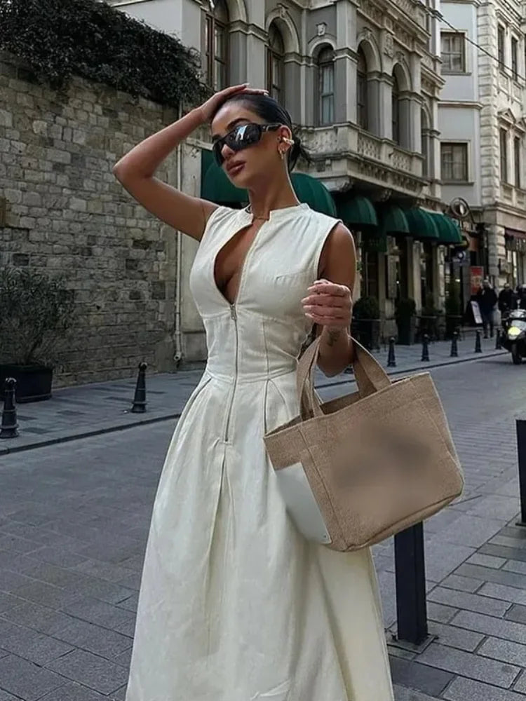Woman in a white dress holding a beige handbag on a city street.
