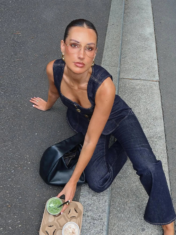 Woman in denim outfit sitting on a street curb with a drink.