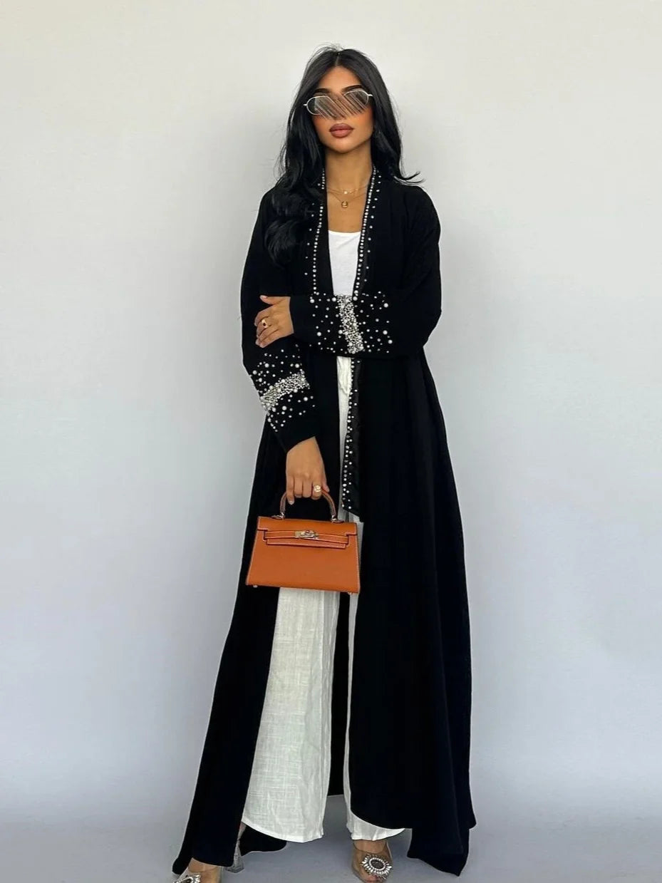 Woman wearing a black abaya with white details and holding a brown handbag against a white background