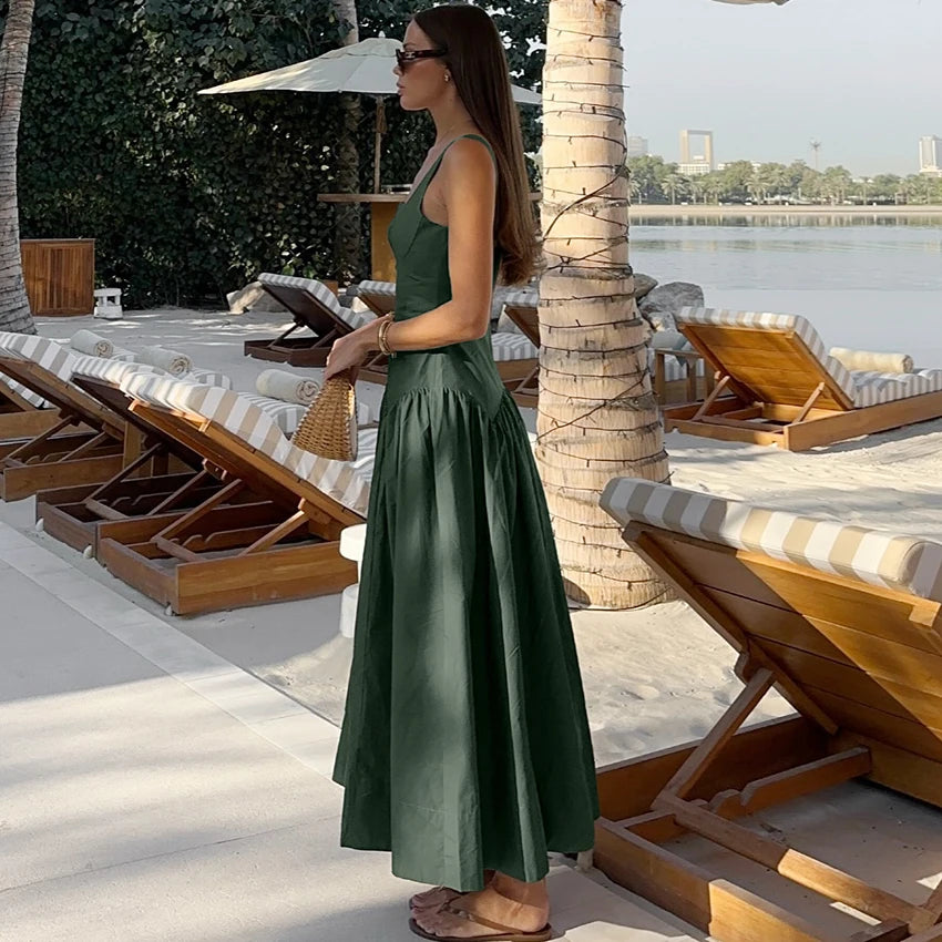 Woman in a green dress standing by lounge chairs by a waterfront.