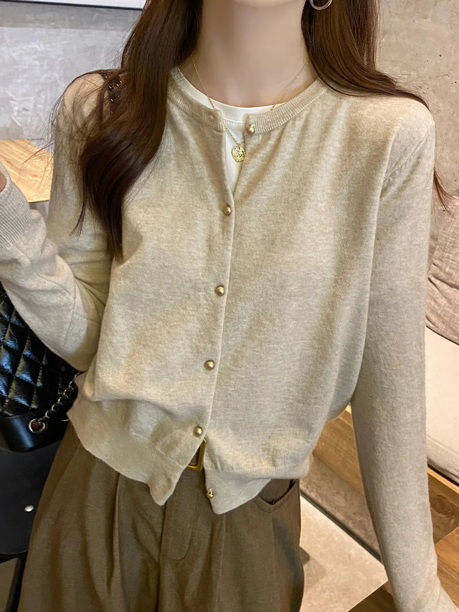Person wearing a beige cardigan with gold buttons indoors.