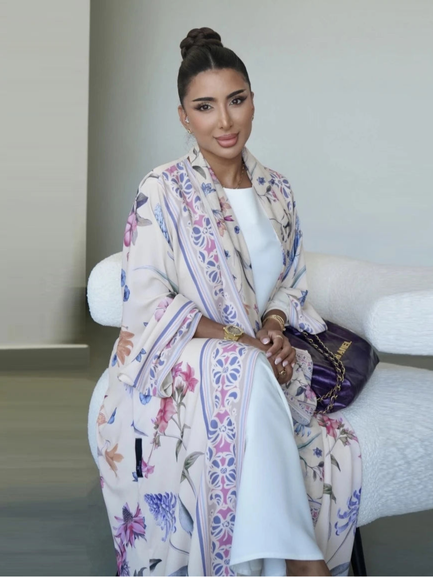 Woman wearing a floral outfit sitting on a white couch with a neutral background