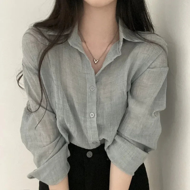 Person wearing a light gray button-up shirt with rolled-up sleeves against a plain background