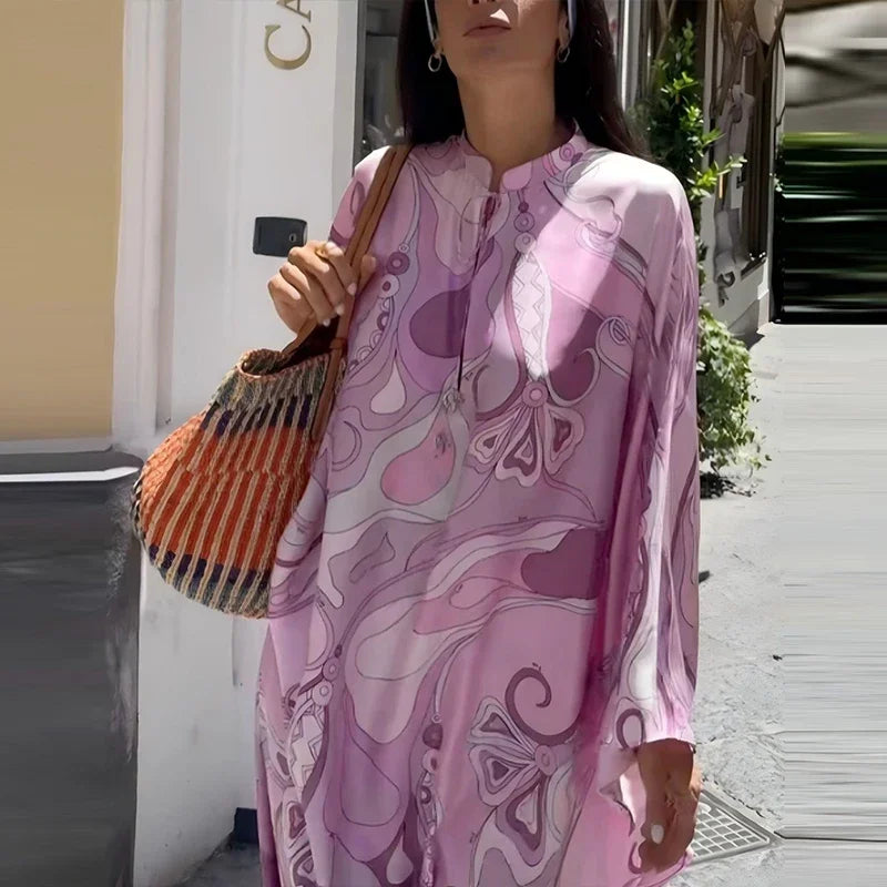 Woman wearing a pink patterned dress holding an orange bag on a city street.