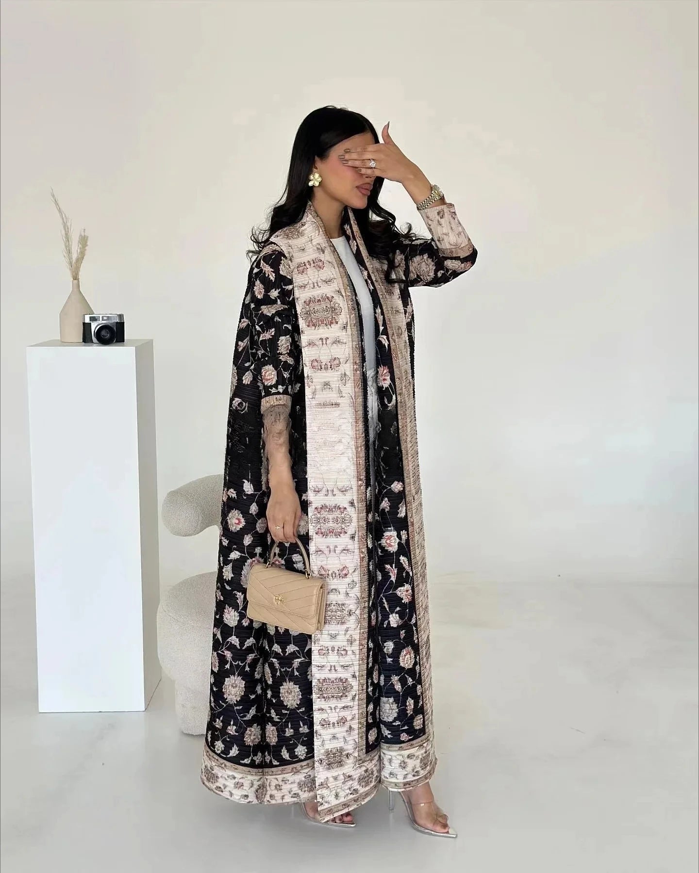 Woman wearing a black and white floral dress with a long jacket against a white background