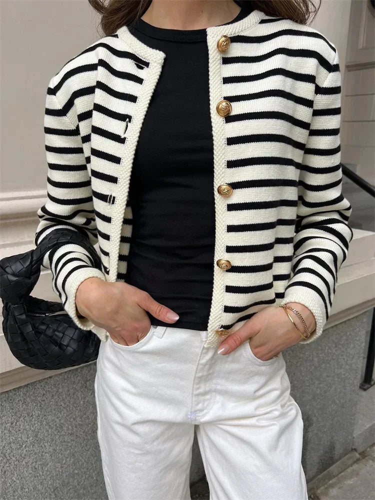 Person wearing a black and white striped cardigan with gold buttons, black top, and white pants.