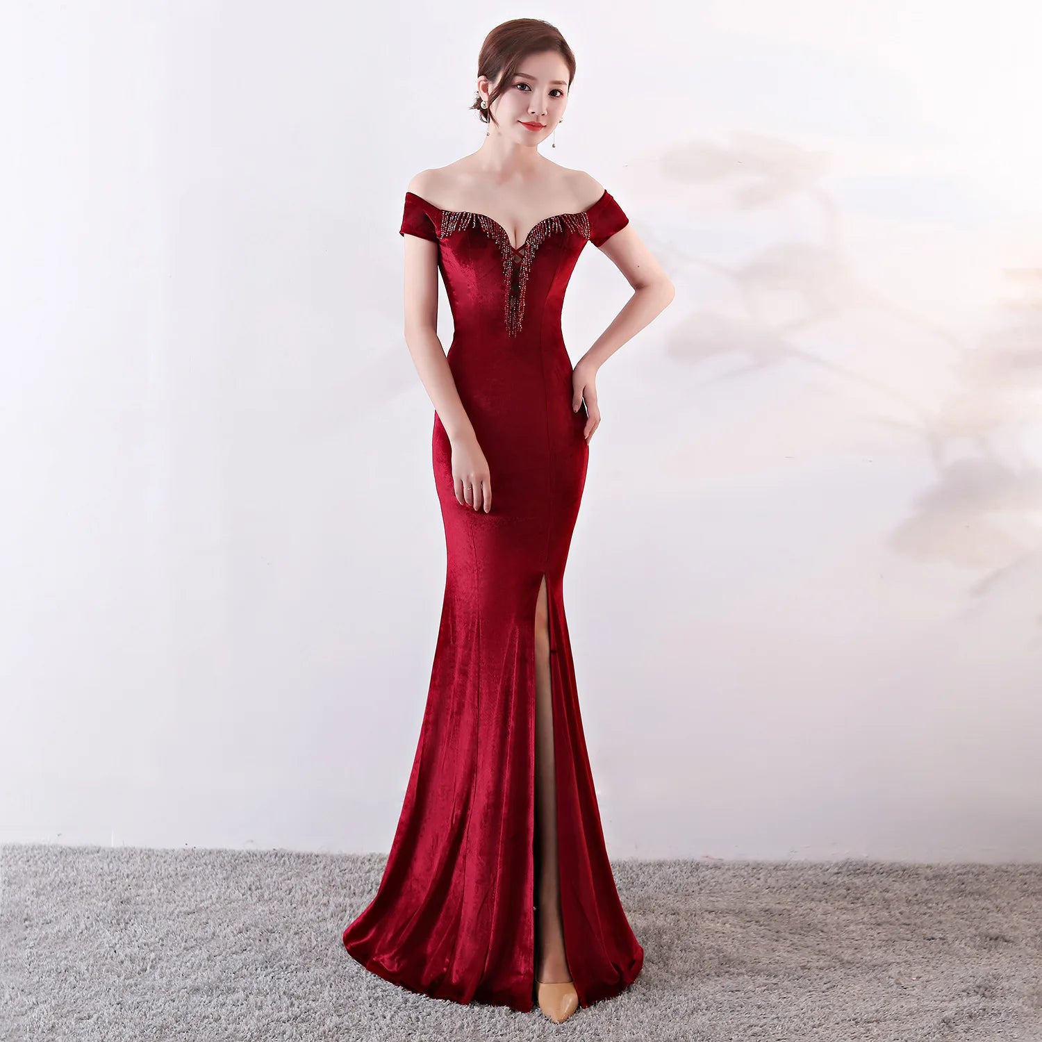 Woman wearing a red off-shoulder evening gown with a slit on a white background