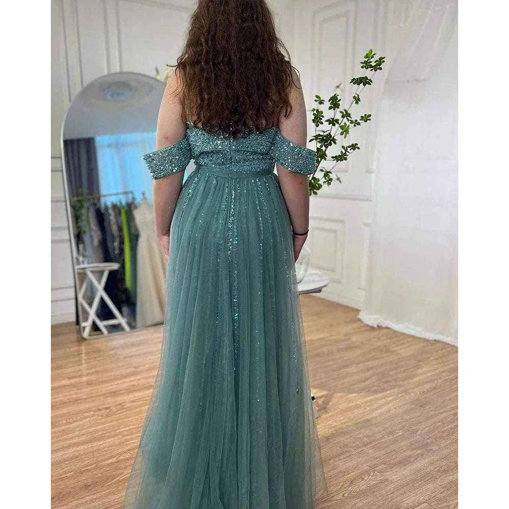 Person wearing a teal off-shoulder gown in a room with a mirror and plant.
