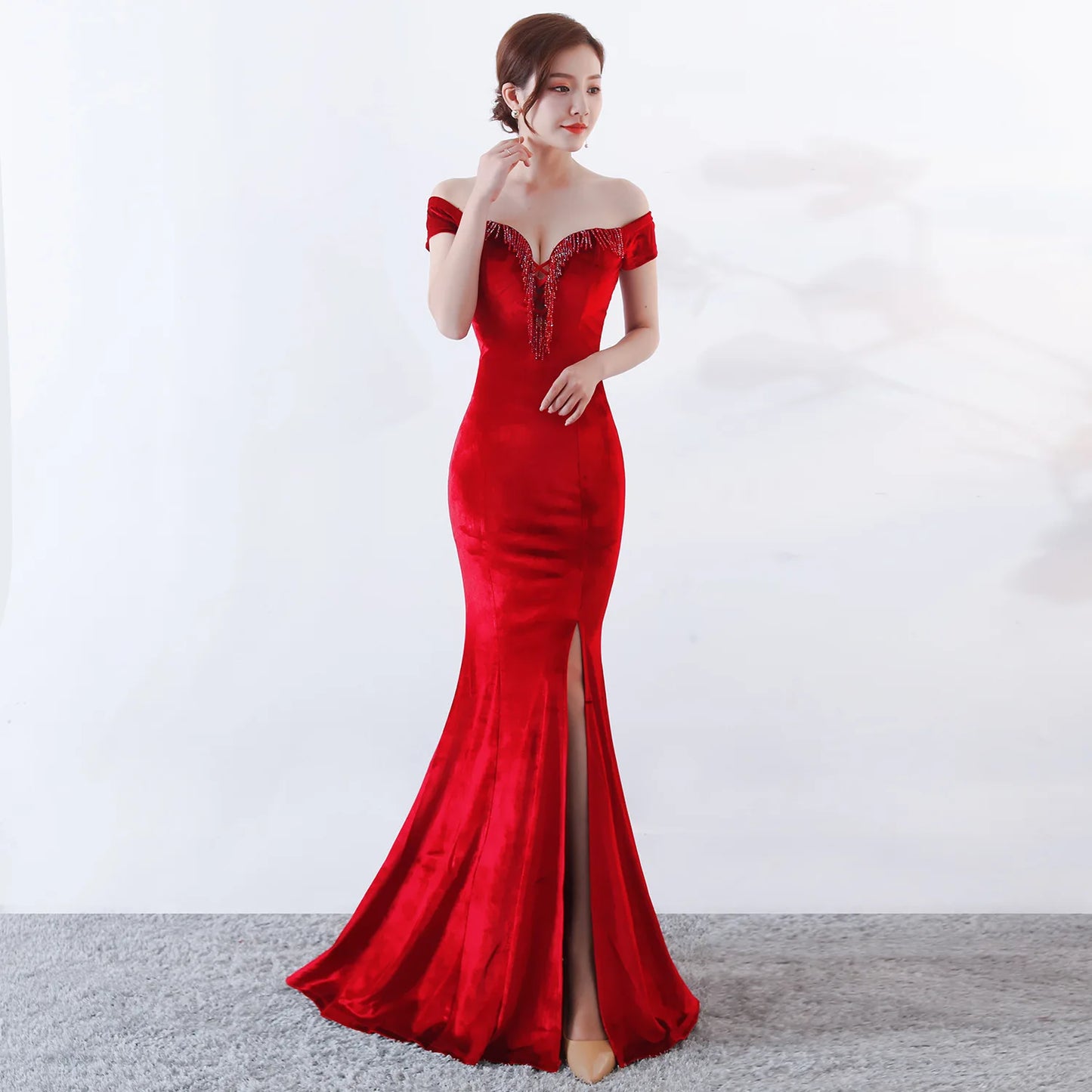 Woman wearing a red off-shoulder evening gown with a slit on a white background