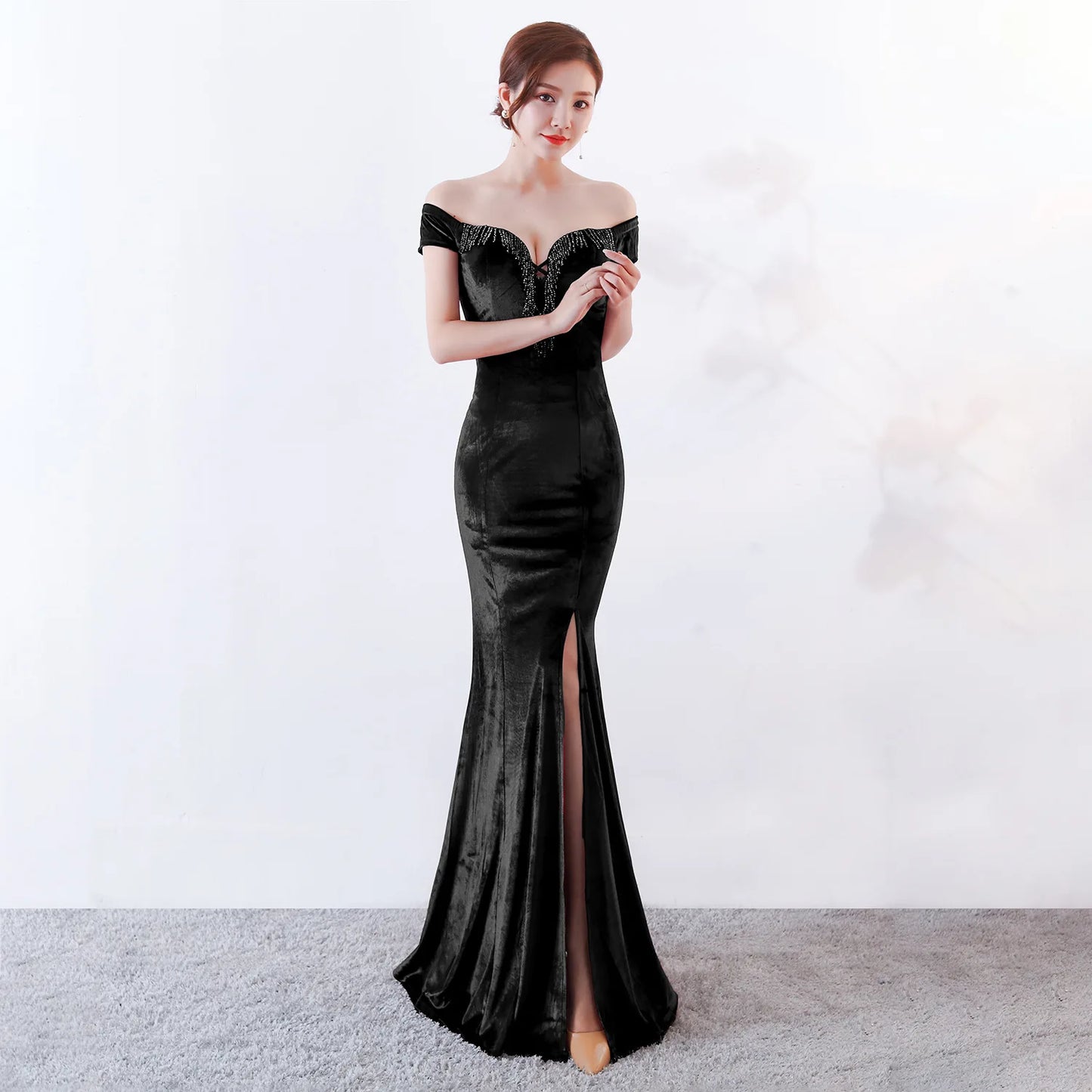Woman wearing a black off-shoulder evening gown with a high slit on a white background