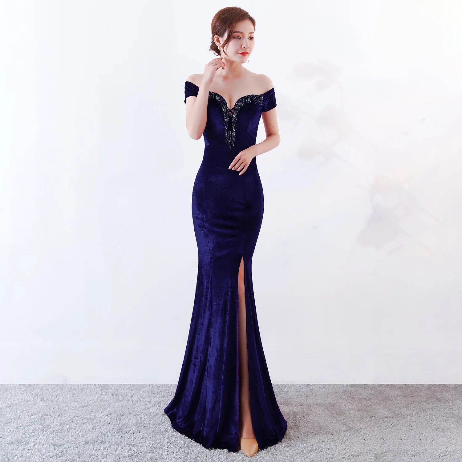 Woman wearing a dark blue off-shoulder evening gown with a high slit on a white background