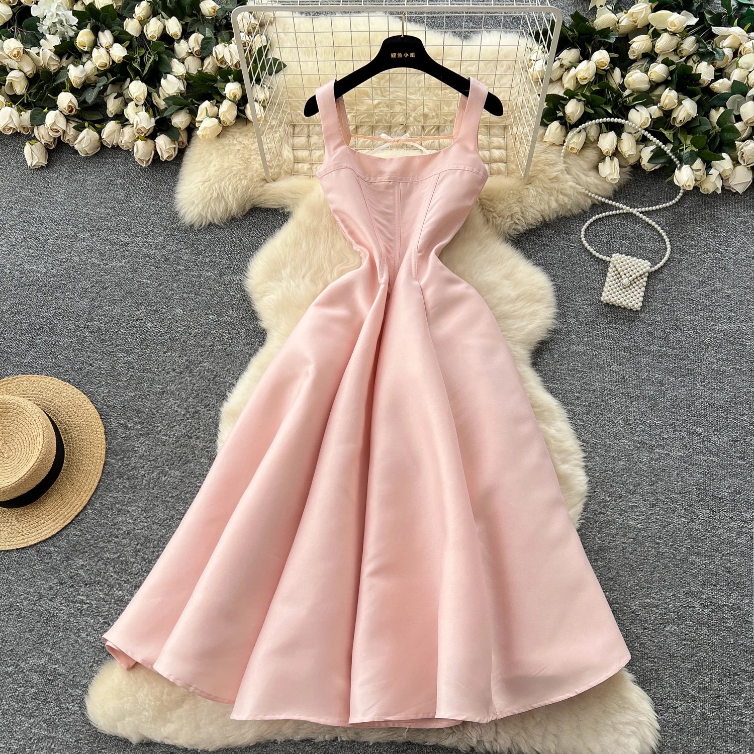 Pink dress on a hanger with decorative flowers and a hat in the background