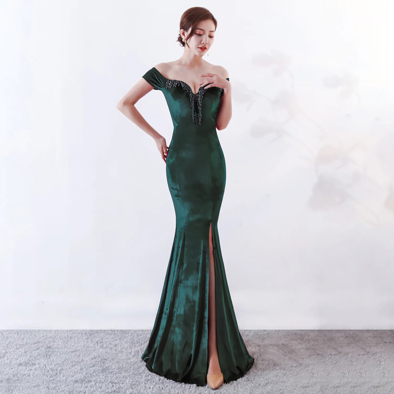 Woman wearing a green evening gown with a slit on a white background