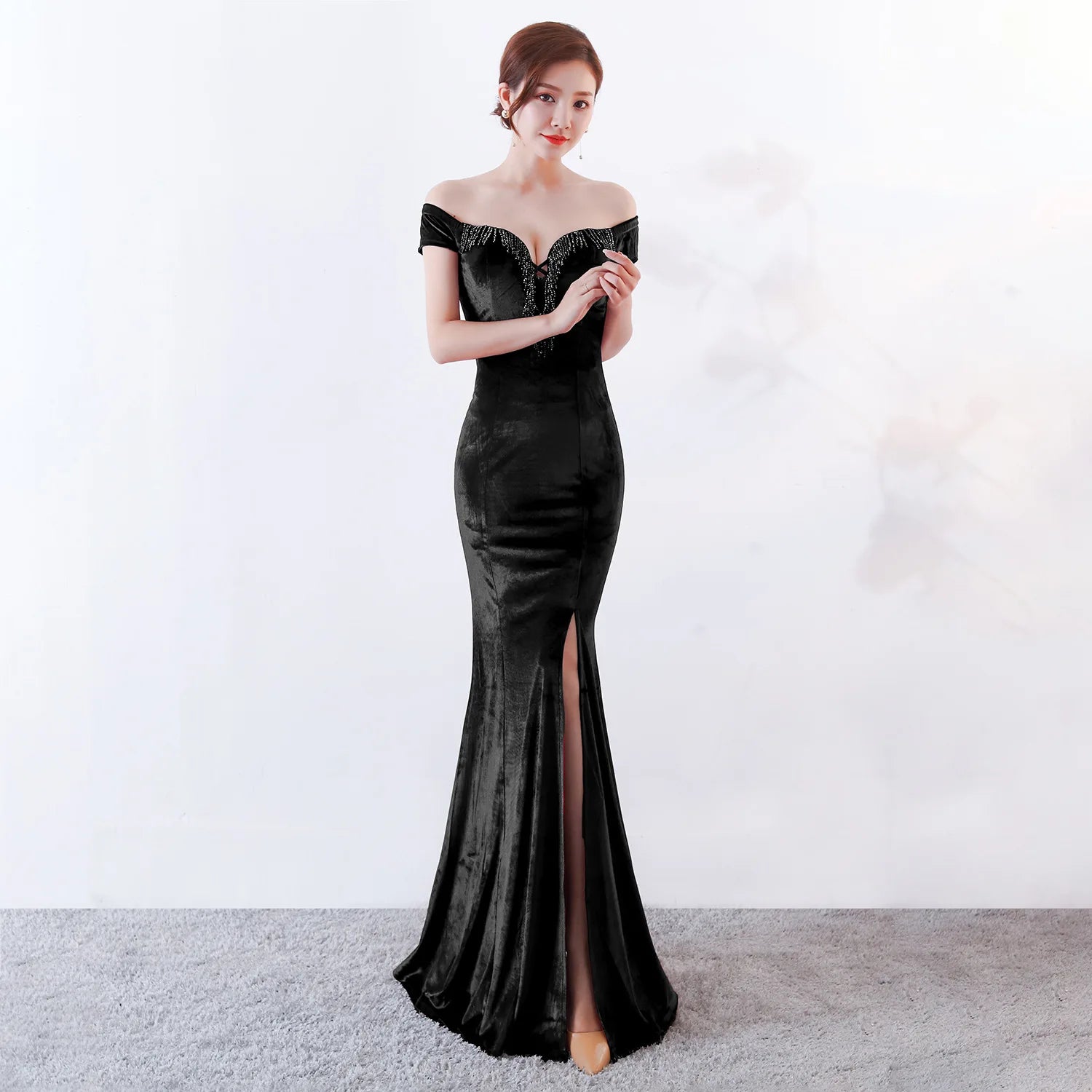 Woman wearing a black off-shoulder evening gown with a high slit on a white background