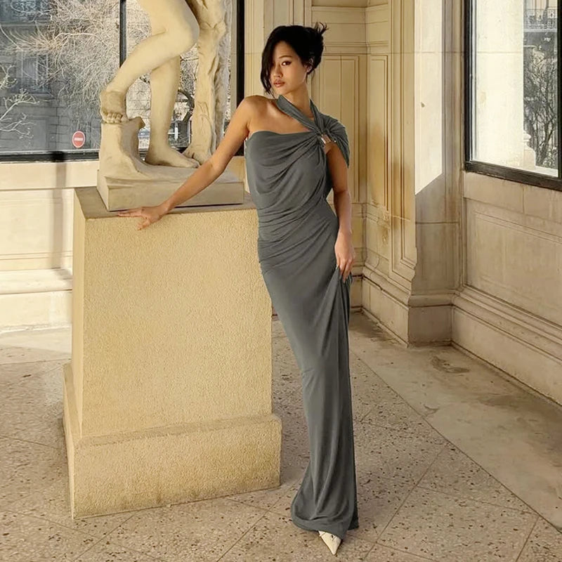 Woman in a gray dress standing next to a classical statue in an elegant interior setting
