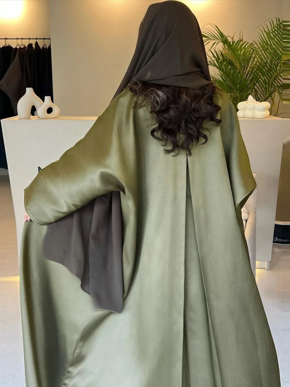 Person wearing a green abaya with a hood in an indoor setting