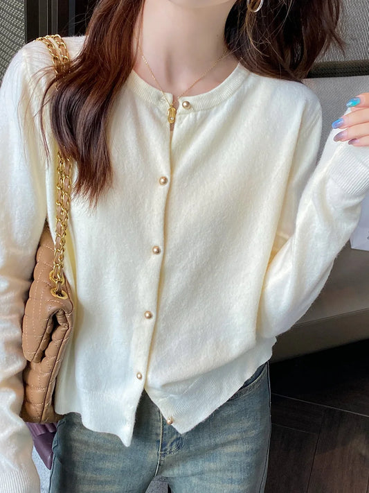 Person wearing a light-colored cardigan with pearl buttons, holding a beige handbag.