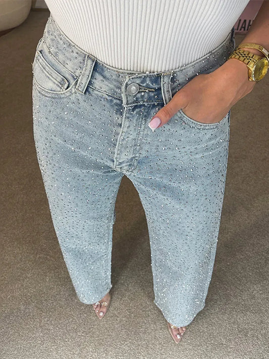 Person wearing light blue jeans with a white top on a neutral background