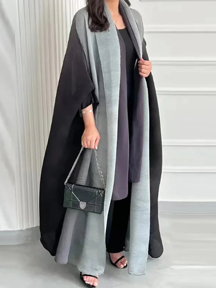Person wearing a long, dark gray coat with a matching scarf in a minimal indoor setting.