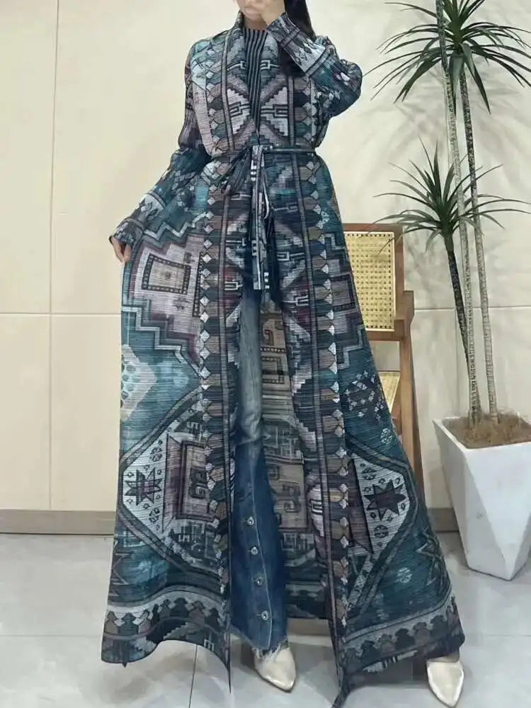Person wearing a long, patterned dress standing indoors with a plant in the background.