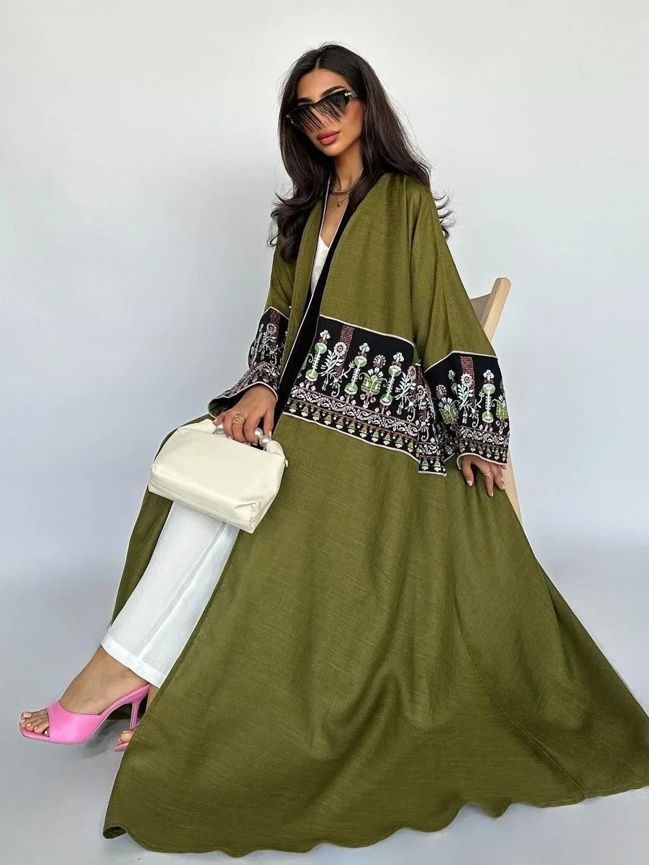 Woman wearing a green dress with black embroidery, white pants, and pink shoes against a white background.