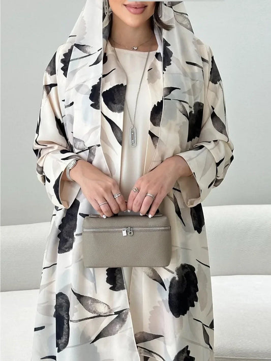 Person wearing a floral-patterned abaya holding a beige handbag against a neutral background