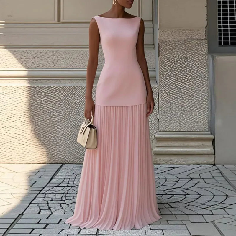 Woman wearing a pink dress standing on a stone pavement with a textured wall in the background.