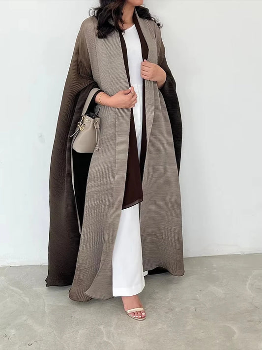 Woman wearing a long brown coat over a white outfit, holding a beige handbag against a white background.