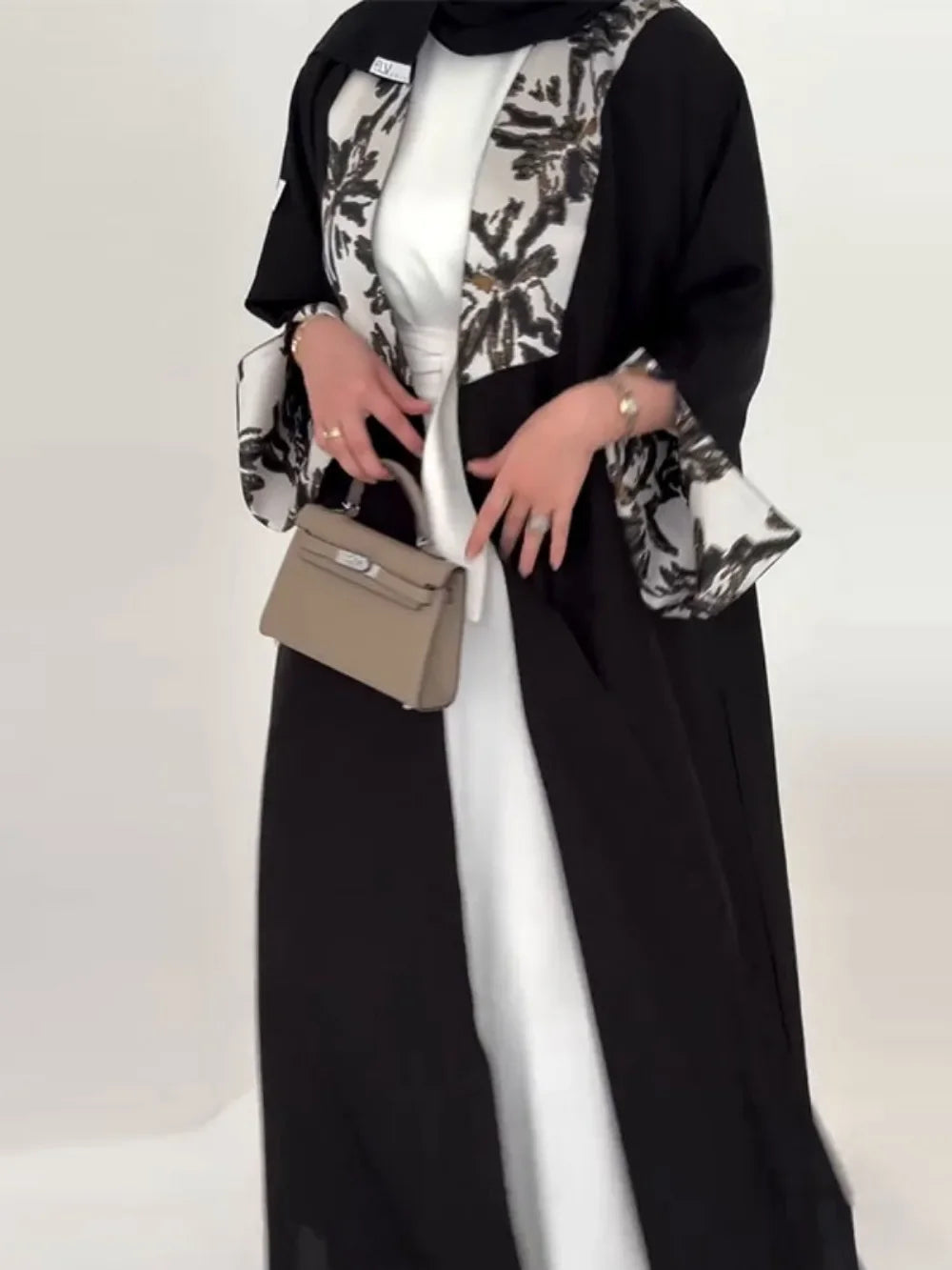 Person wearing a black outfit with a patterned scarf and holding a beige handbag on a white background