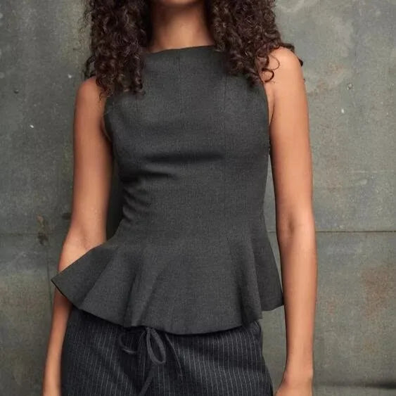 Woman wearing a dark gray peplum top against a textured gray background