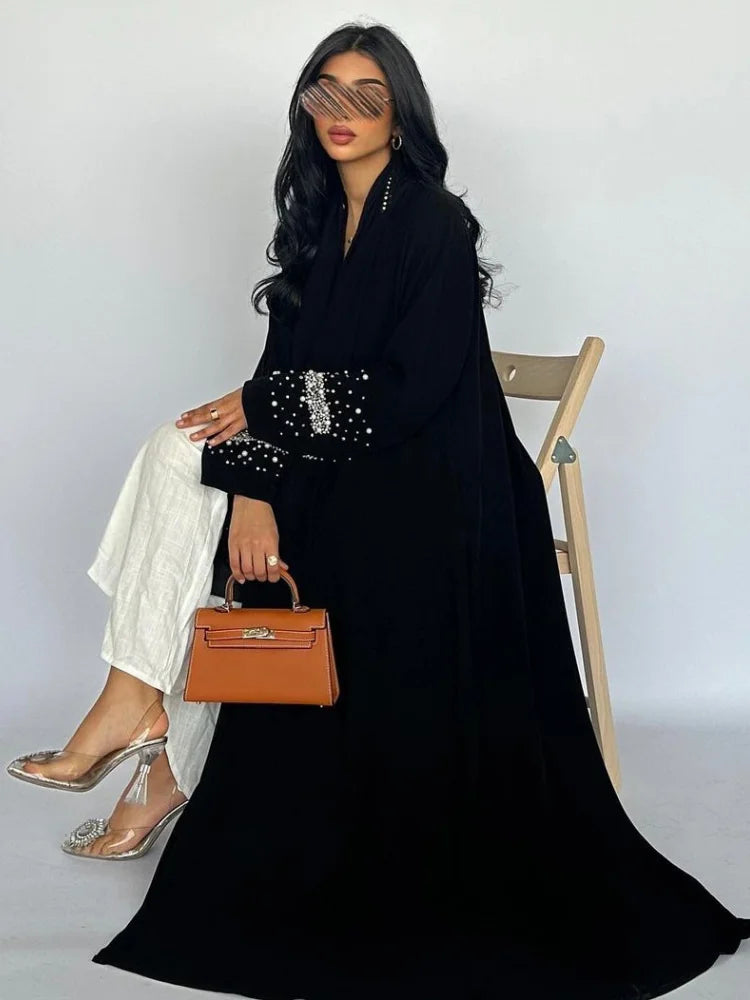 Woman in a black outfit with a brown handbag sitting on a chair against a white background