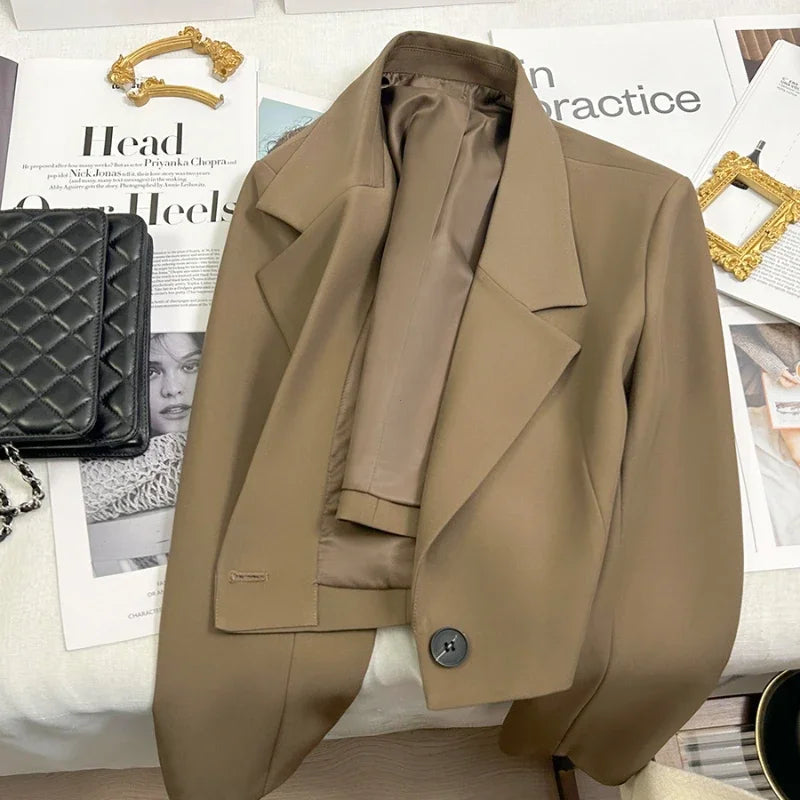 Beige blazer on a surface with a magazine and black handbag in the background