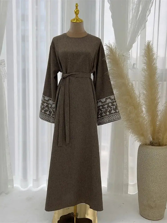 Brown dress with patterned cuffs on a mannequin against a white curtain background