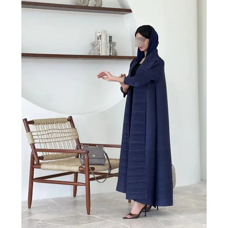 Woman in a long dark blue dress standing in a room with a chair and shelves.