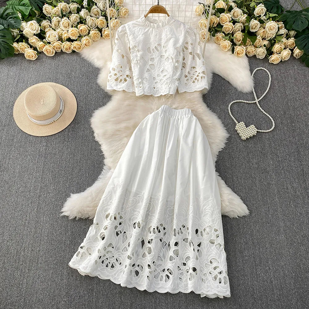 White lace top and skirt set with a hat and handbag on a textured surface.