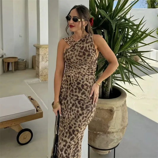 Woman in a leopard print dress standing next to a large potted plant indoors.