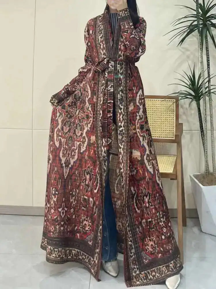 Person wearing a long, patterned coat in an indoor setting with a plant in the background.