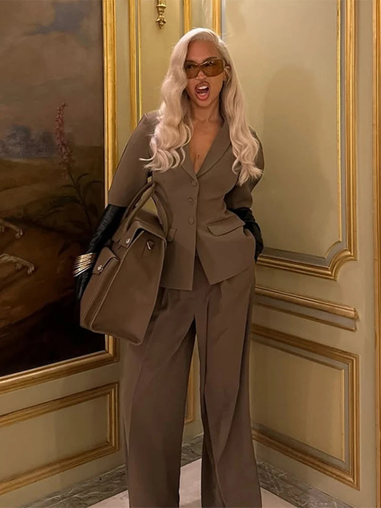 Person in a beige suit with sunglasses and gloves standing in an ornate room.