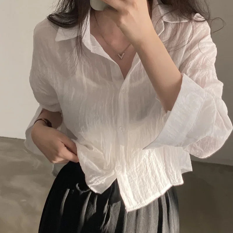 Person wearing a white blouse with ruffled sleeves against a neutral background