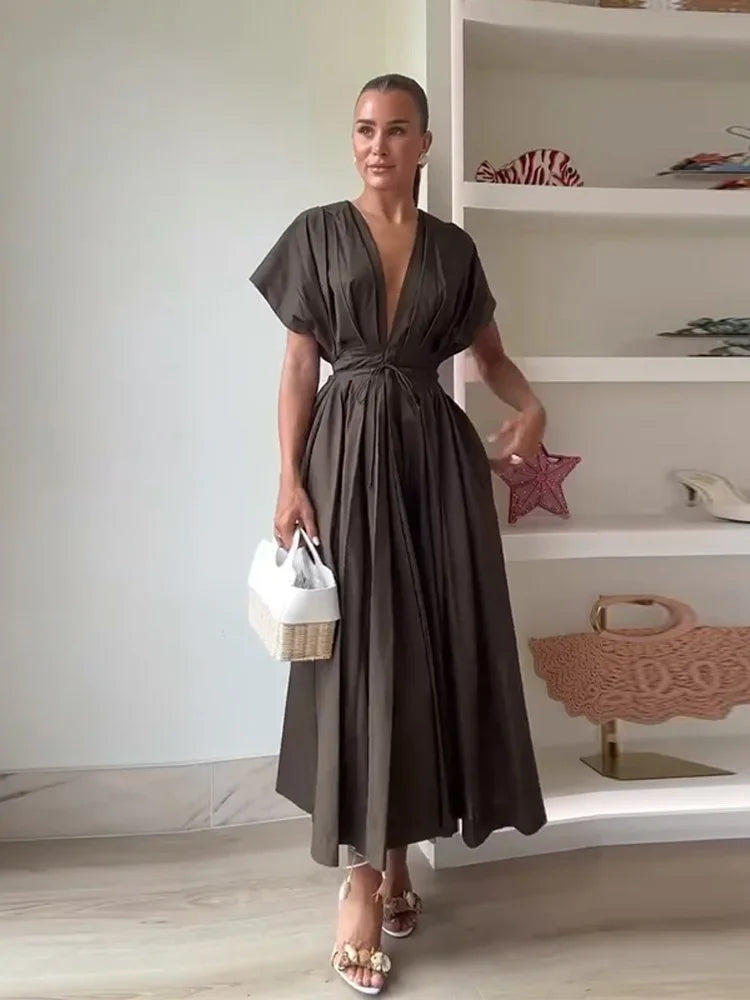Woman in a brown dress holding a white bag in a room with shelves.