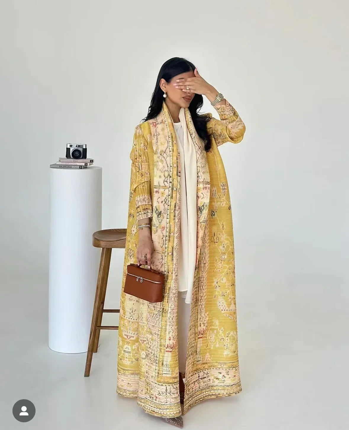 Woman wearing a long, patterned yellow garment with a white background